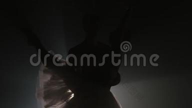 专业芭蕾舞情侣在聚光灯下跳舞，在大舞台上抽烟。 美丽的年轻女子，<strong>还有</strong>一个穿着泛光灯的男人